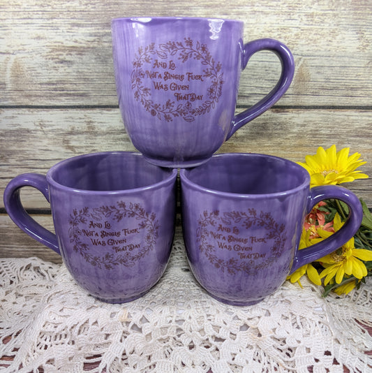 Three purple mugs with engraved text on a lace tablecloth with flowers.