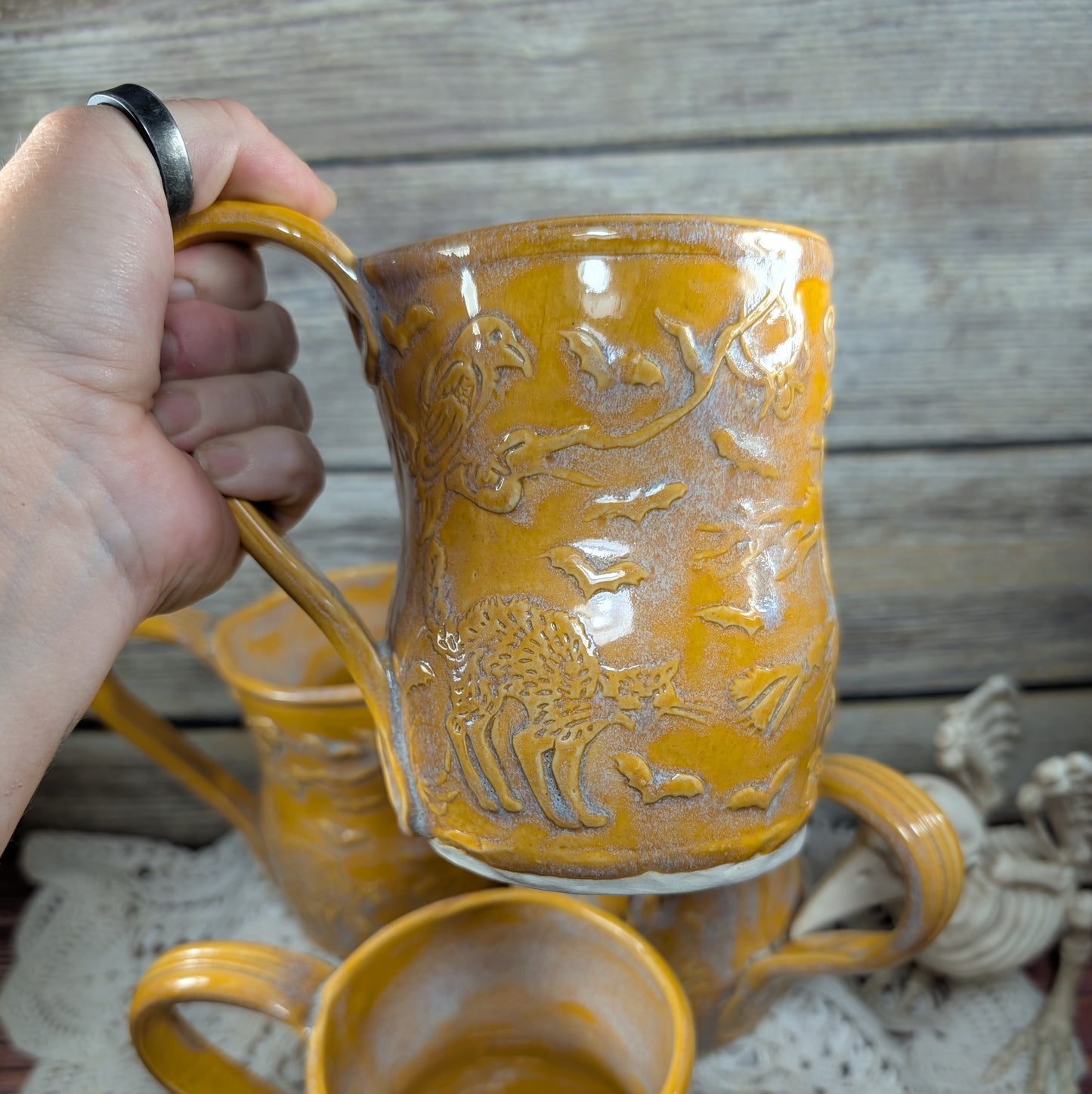 Hand holding a yellow ceramic mug with embossed design against a wooden background