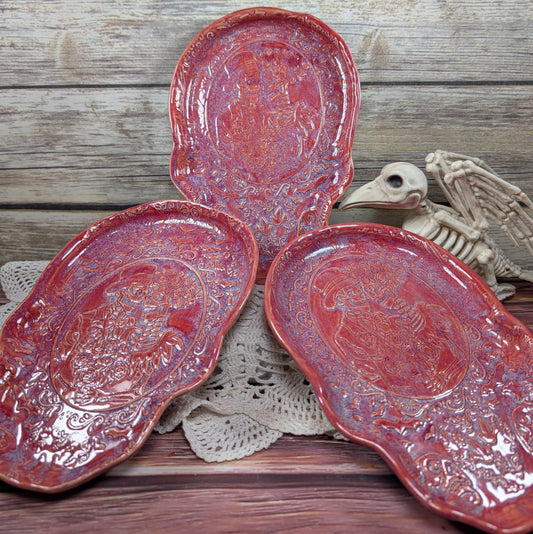 Three red ceramic dishes on a wooden surface with a skeleton hand and doily in the background.