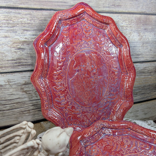 Decorative red plate with intricate patterns on a wooden surface with a skeleton hand.