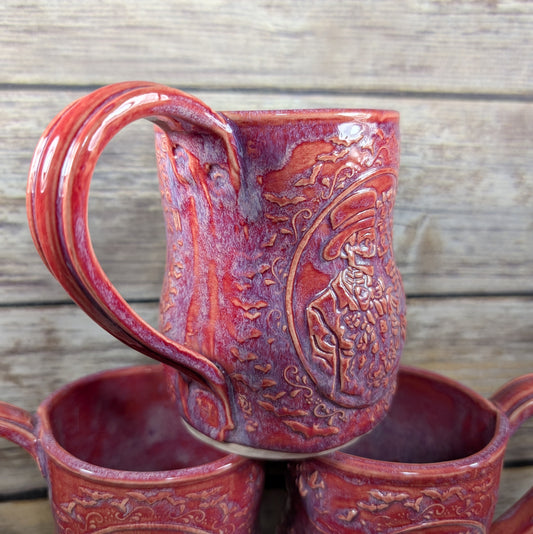 Red ceramic mug with embossed design on a wooden surface
