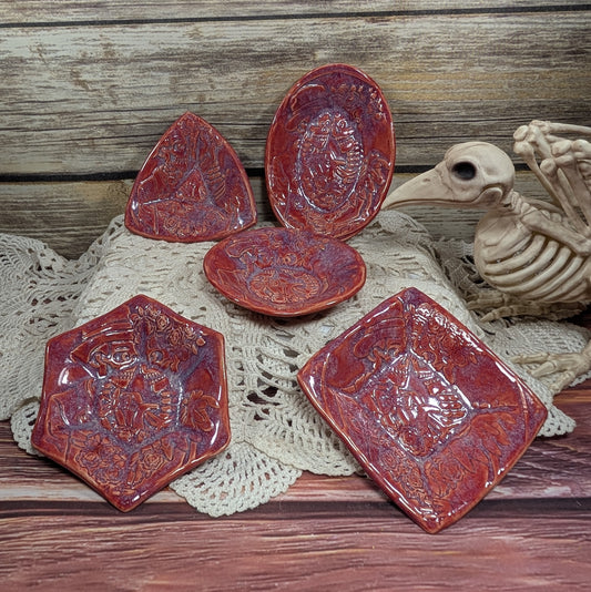 Set of red ceramic dishes with embossed designs on a wooden surface with a skeleton and doily.