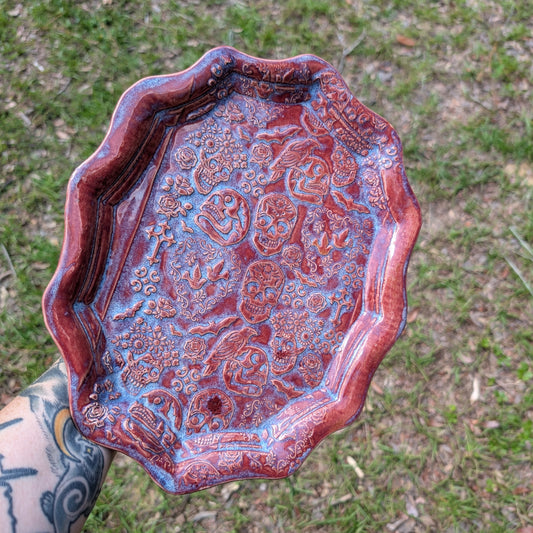 Ceramic tray with skull design held by a person against a grassy background
