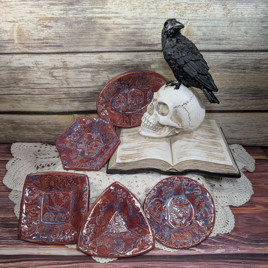 Decorative dishes displayed on a skull, book, and crow on a wooden surface.