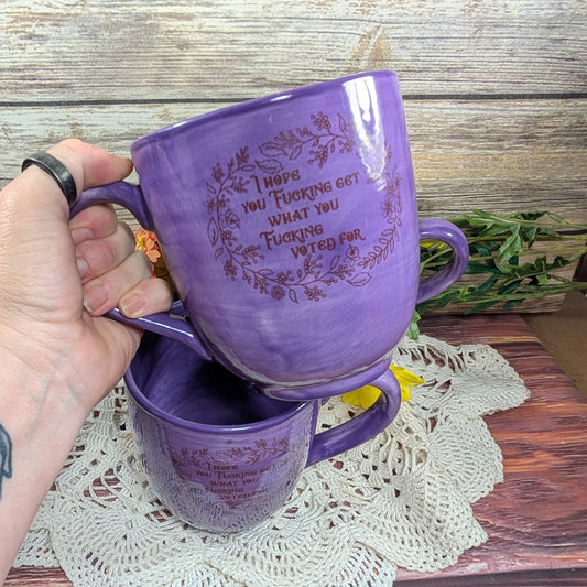 Purple mugs with text held by a hand on a wooden surface with a doily.