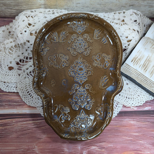 Decorative brown ceramic tray with floral patterns on a wooden surface with a lace doily.