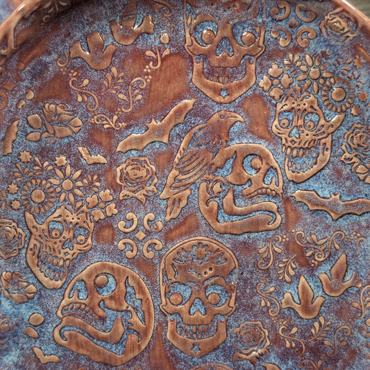 Decorative metal surface with engraved skull, bird, and floral patterns.