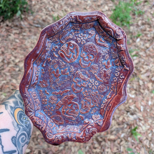 Decorative metal tray with intricate designs held by a person outdoors.