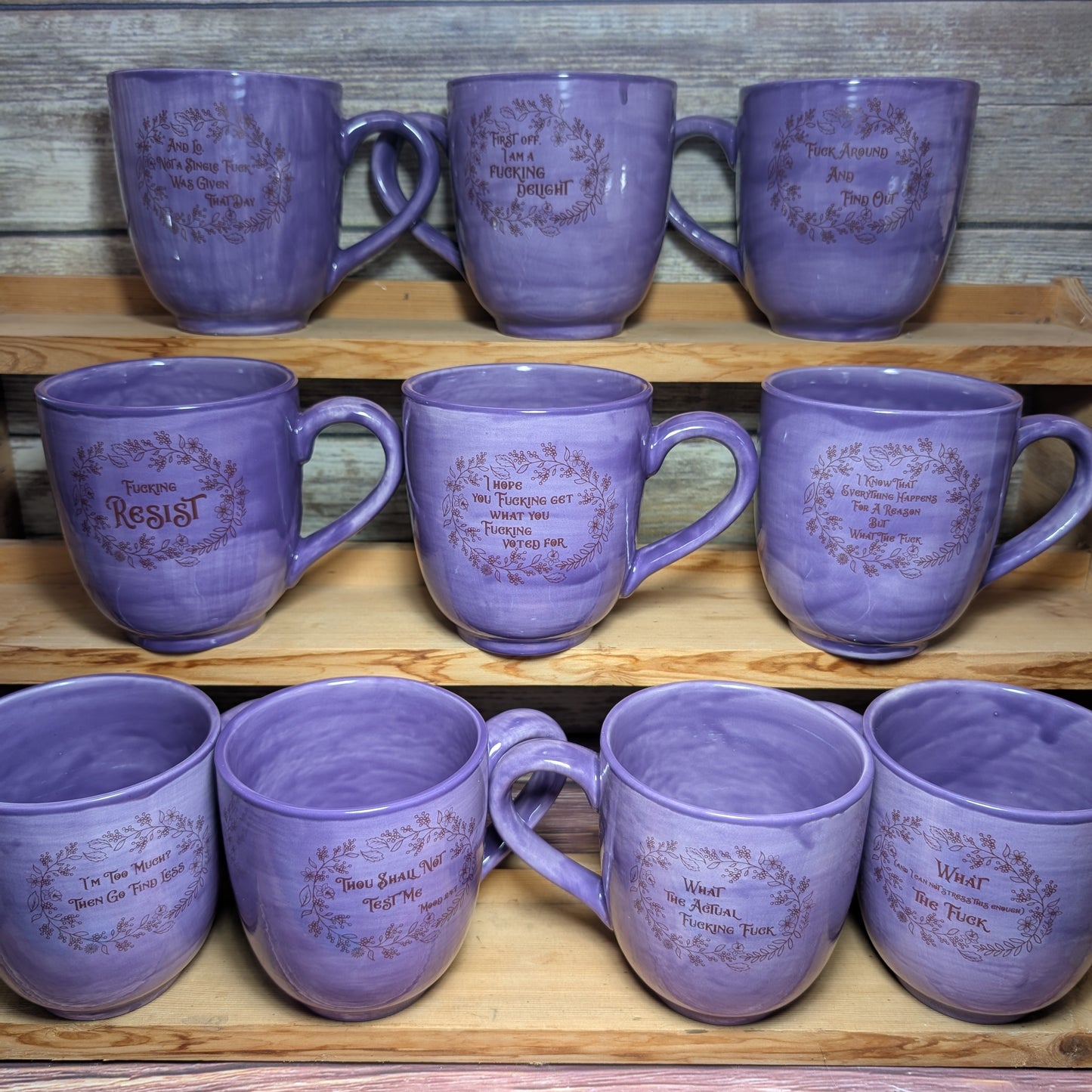 Set of purple mugs with text on a wooden shelf