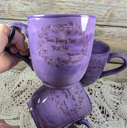 Purple mug with humorous text held by a hand on a wooden surface.