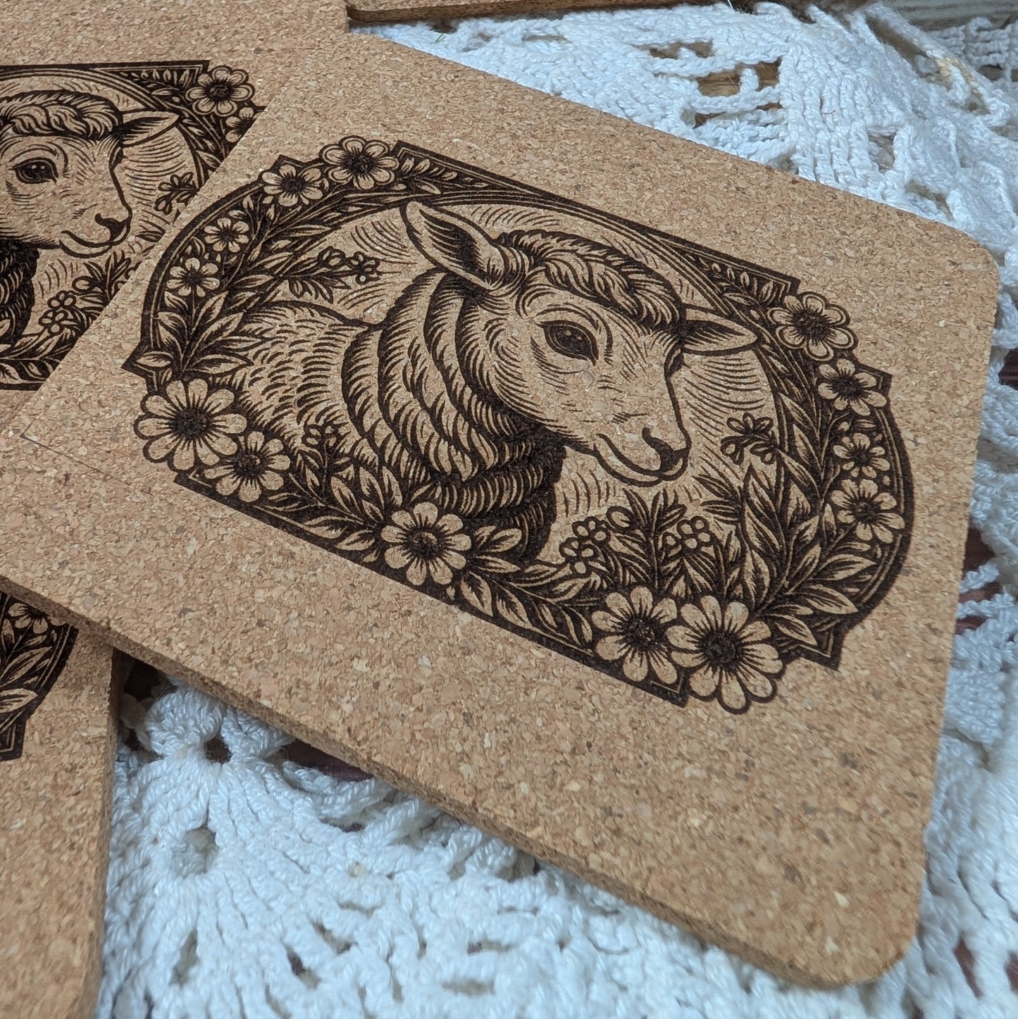 Cork coaster with engraved goat design on a lace background