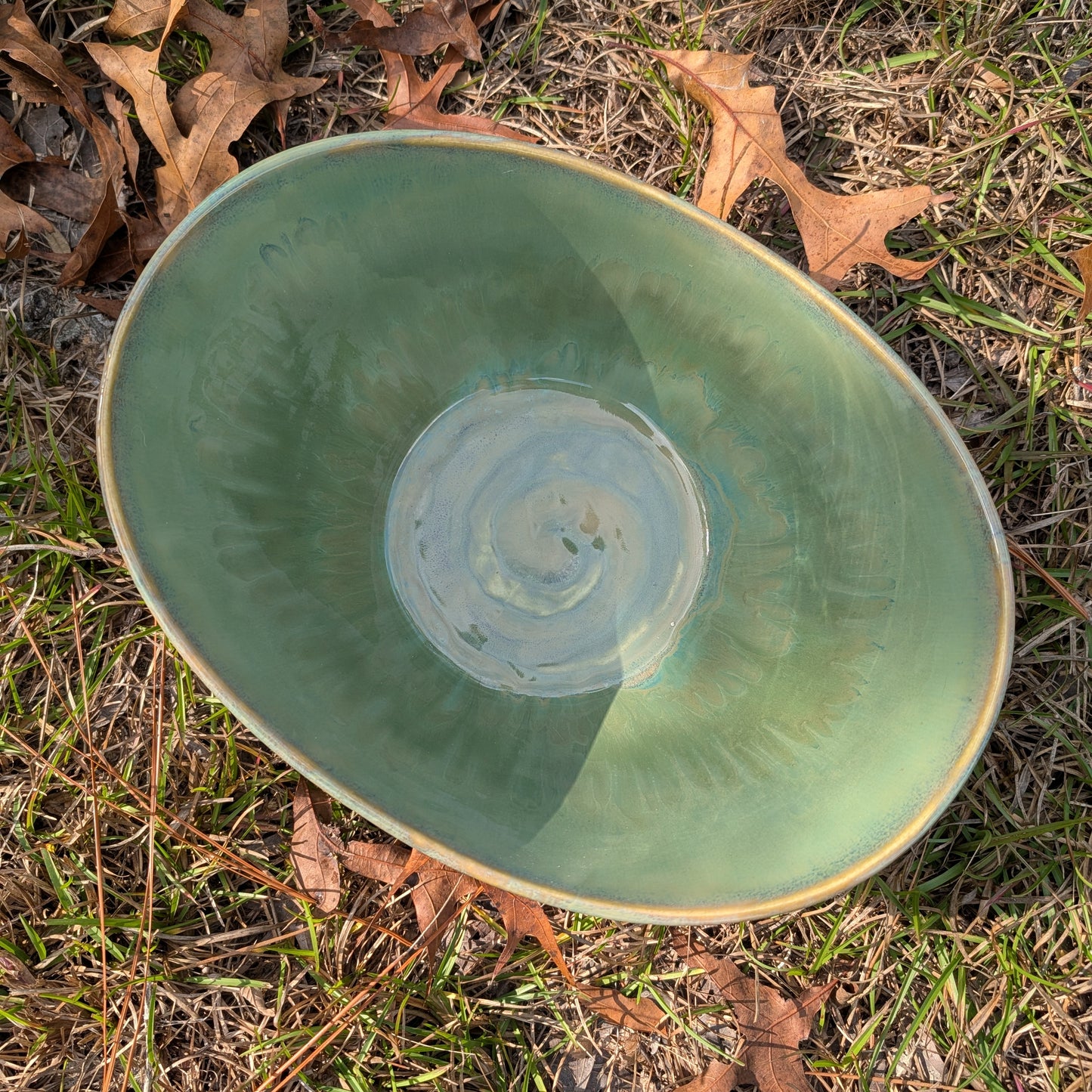 Green ceramic bowl on grass with leaves