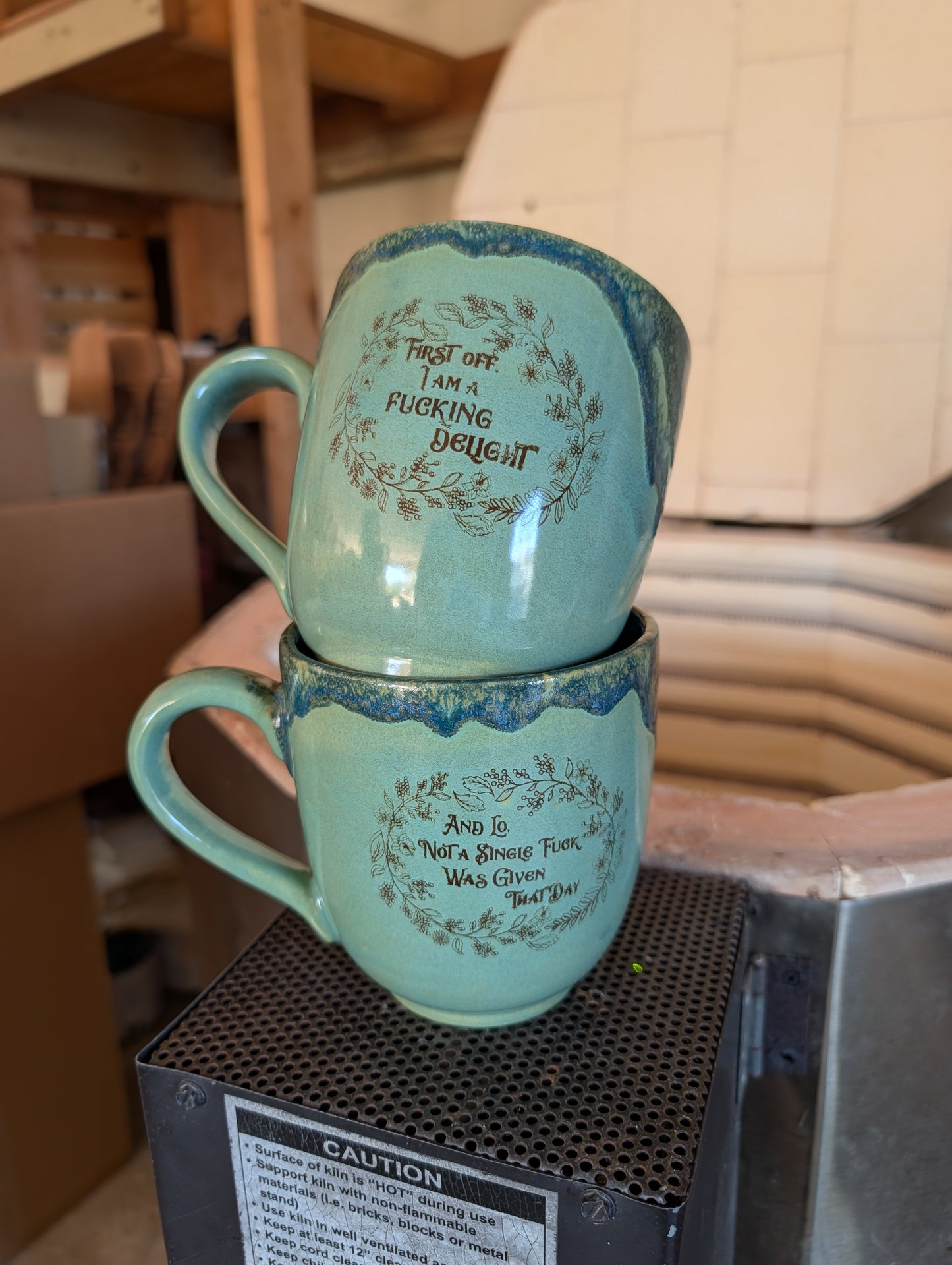 Two stacked teal mugs with text on a black surface