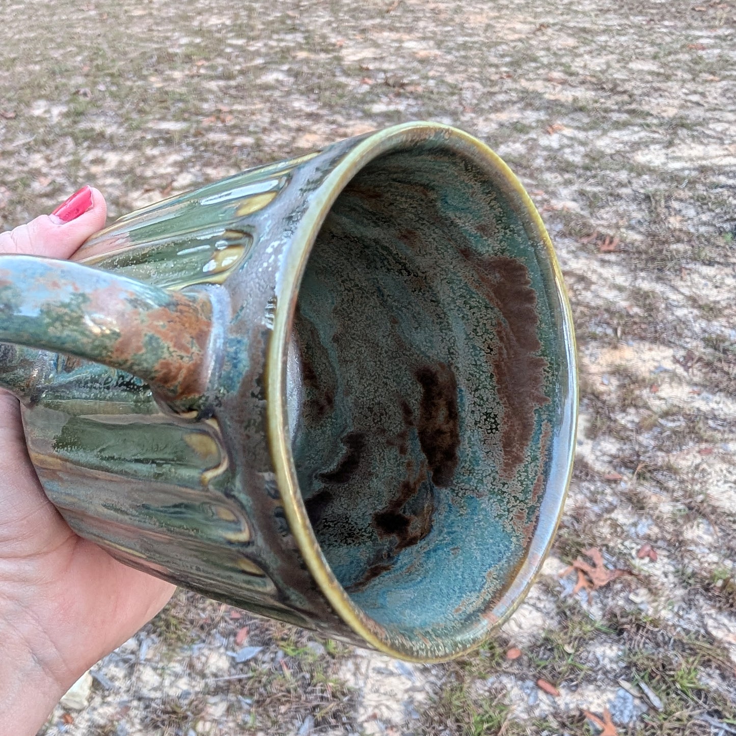 Hand holding a ceramic mug with a textured surface against a natural background