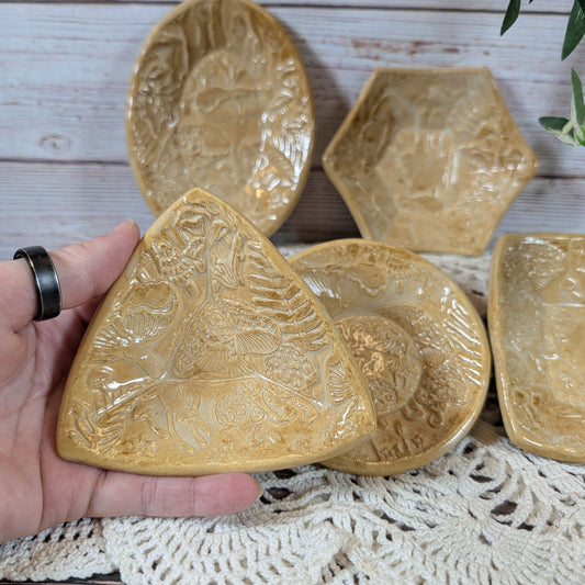 A hand holding a small triangular dish. In back is the rest of the set of small ceramic trinket dishes, decorated with a mushroom motif, on a lace doily with a wooden background
