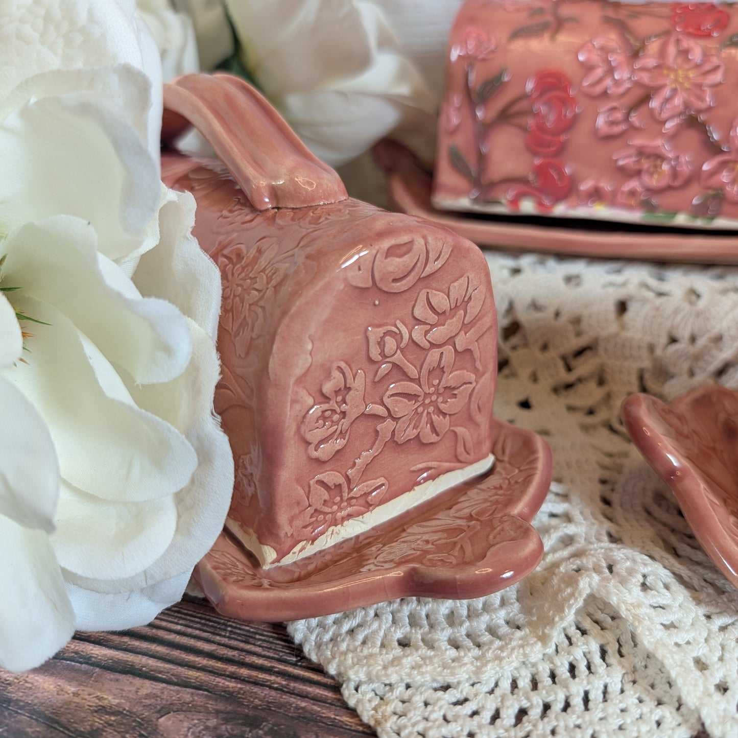 Pink ceramic butter dish with floral design on a lace tablecloth