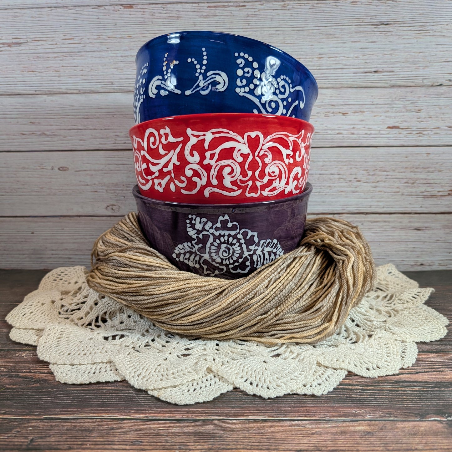Stack of ceramic yarn bowls with decorative patterns on a wooden surface with beige yarn.
