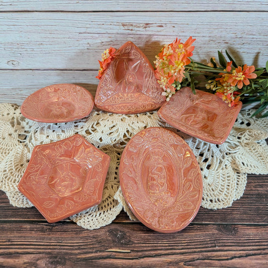 Five pink trinket dishes on a lace doily on a wooden surface, with flowers. 