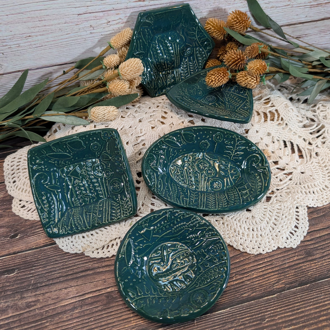 A selection of green trinket dishes on a crocheted doily on a wooden surface.
