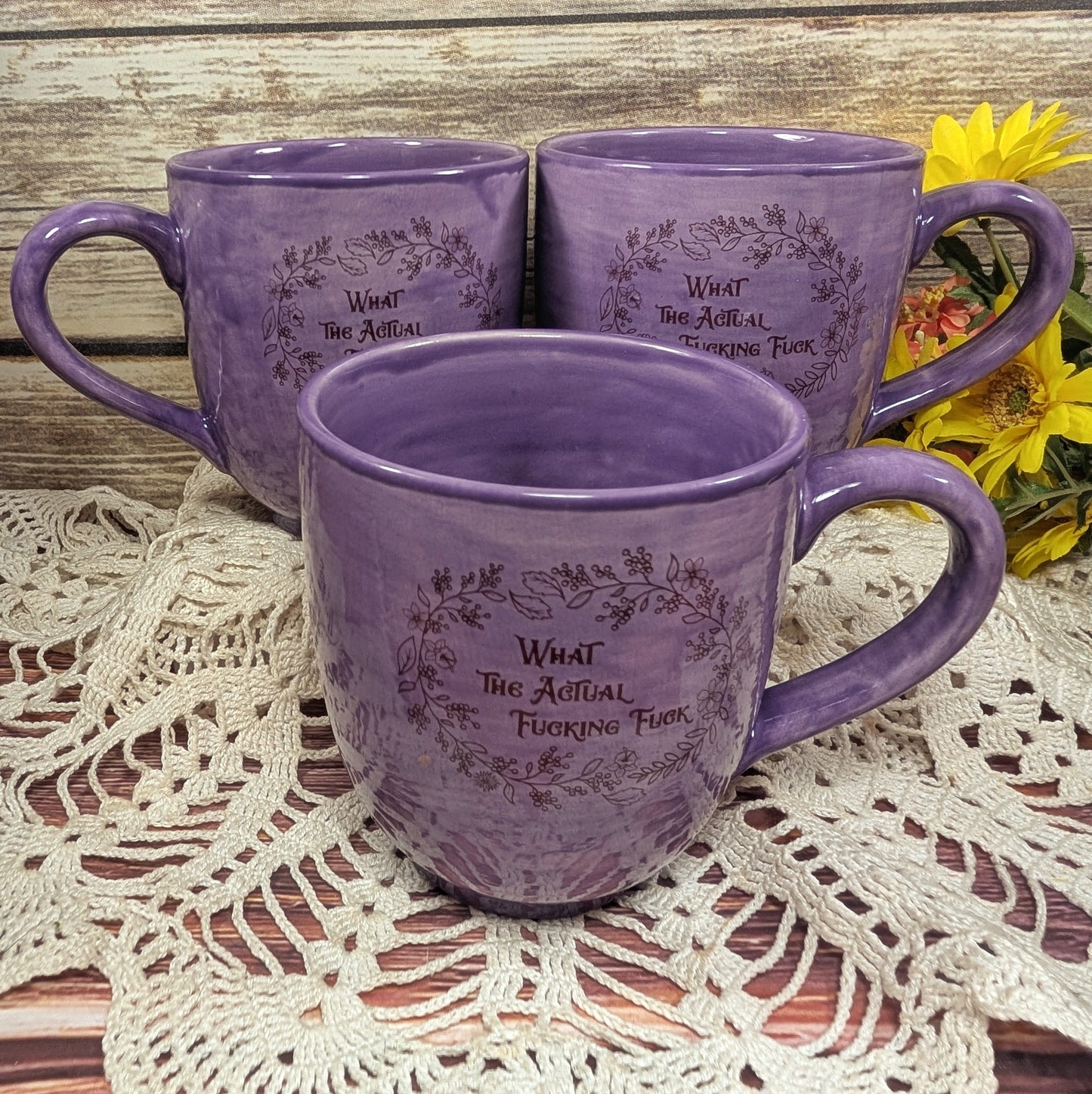 Three purple mugs with text on a lace tablecloth