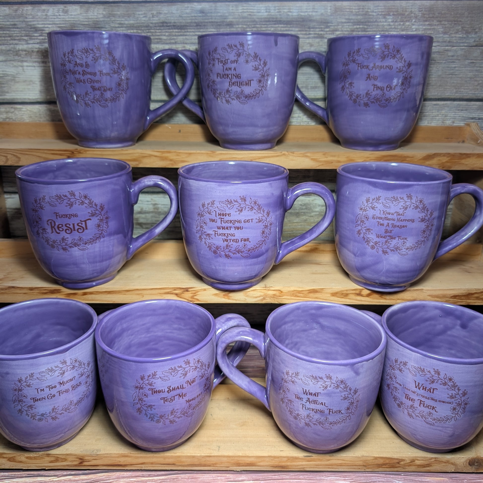 Set of purple mugs with text on a wooden shelf