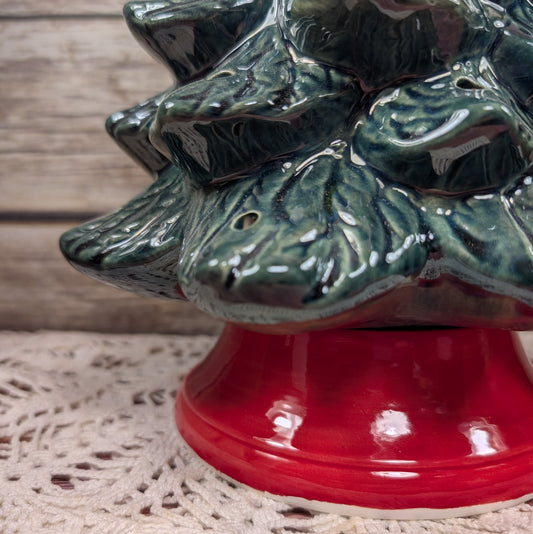 Decorative ceramic piece with green leaves and a red base on a textured surface