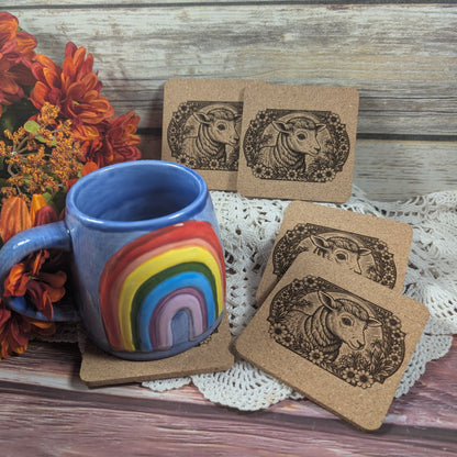 Blue mug with rainbow design on a wooden surface with floral decorations and coasters featuring sheep illustrations.