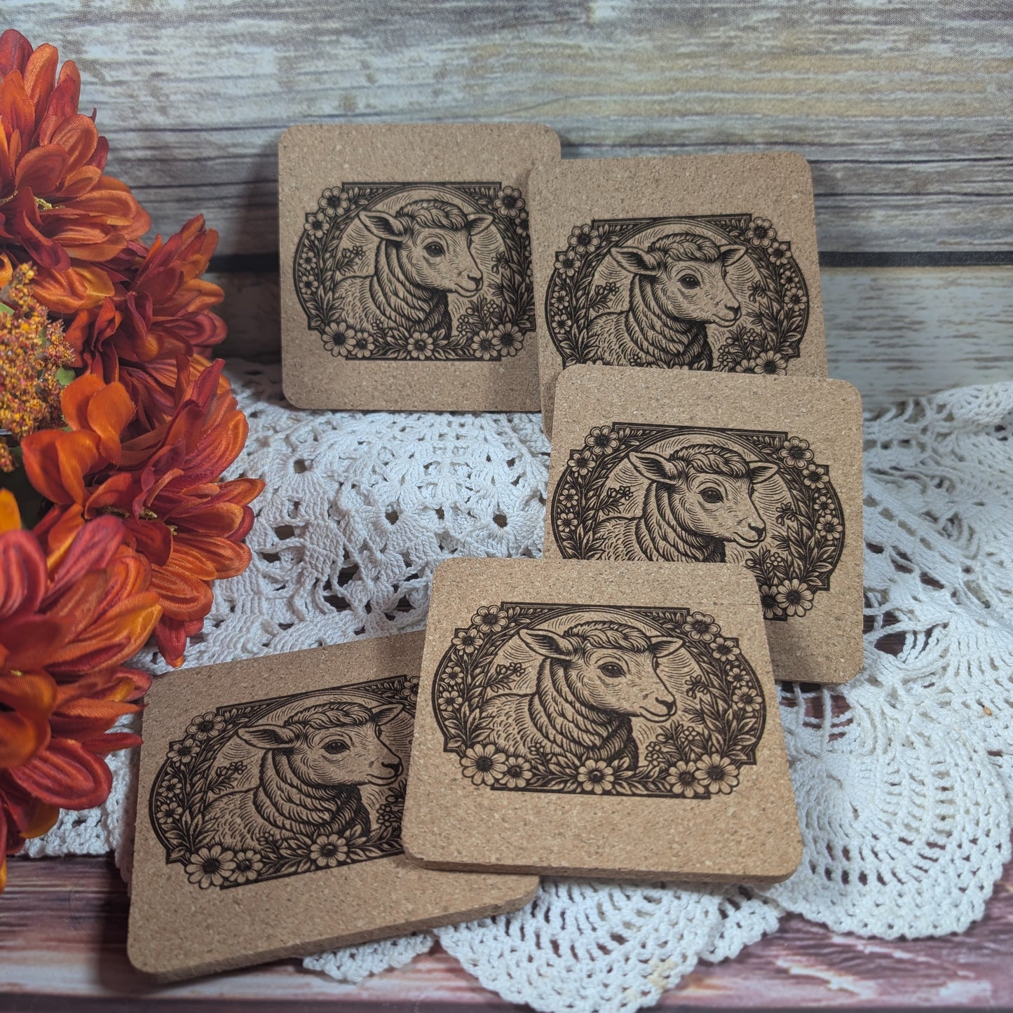 Set of brown coasters with sheep design on a lace tablecloth with flowers.