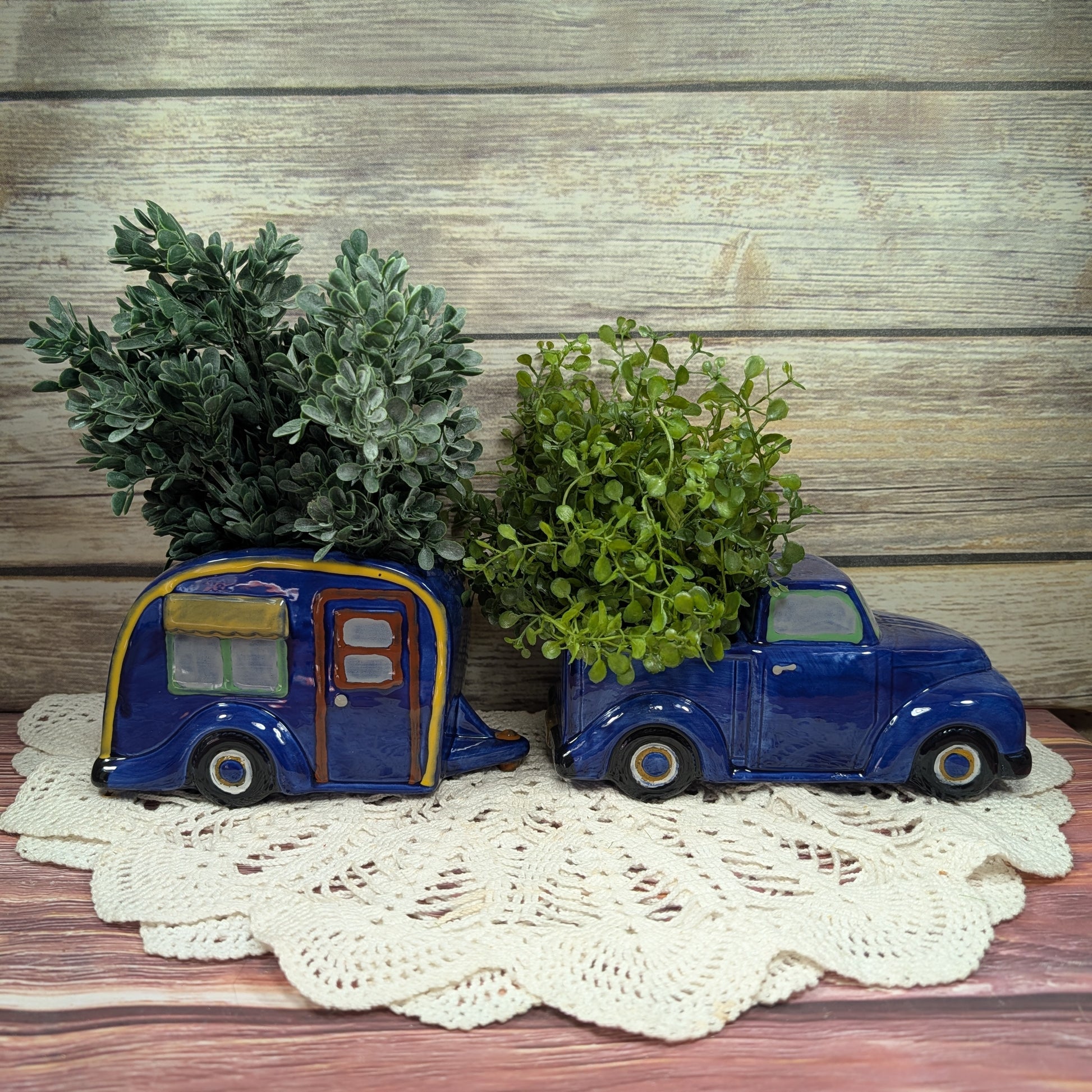 Two blue vintage-style car planters with green plants on a wooden surface.
