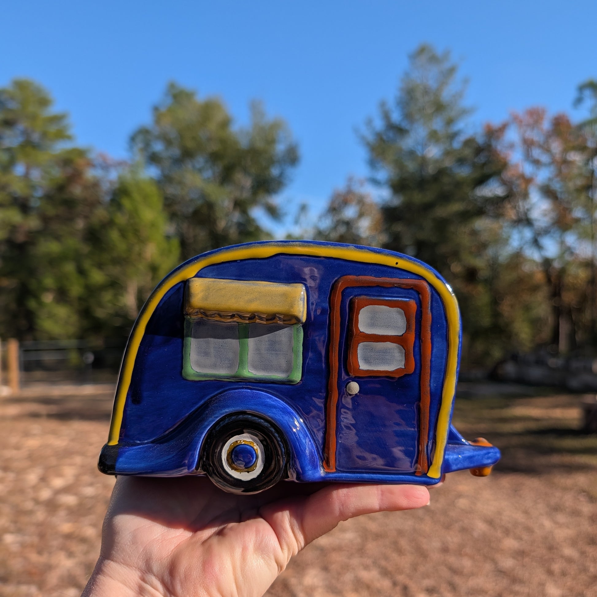 Blue camper planter held in a hand with trees in the background