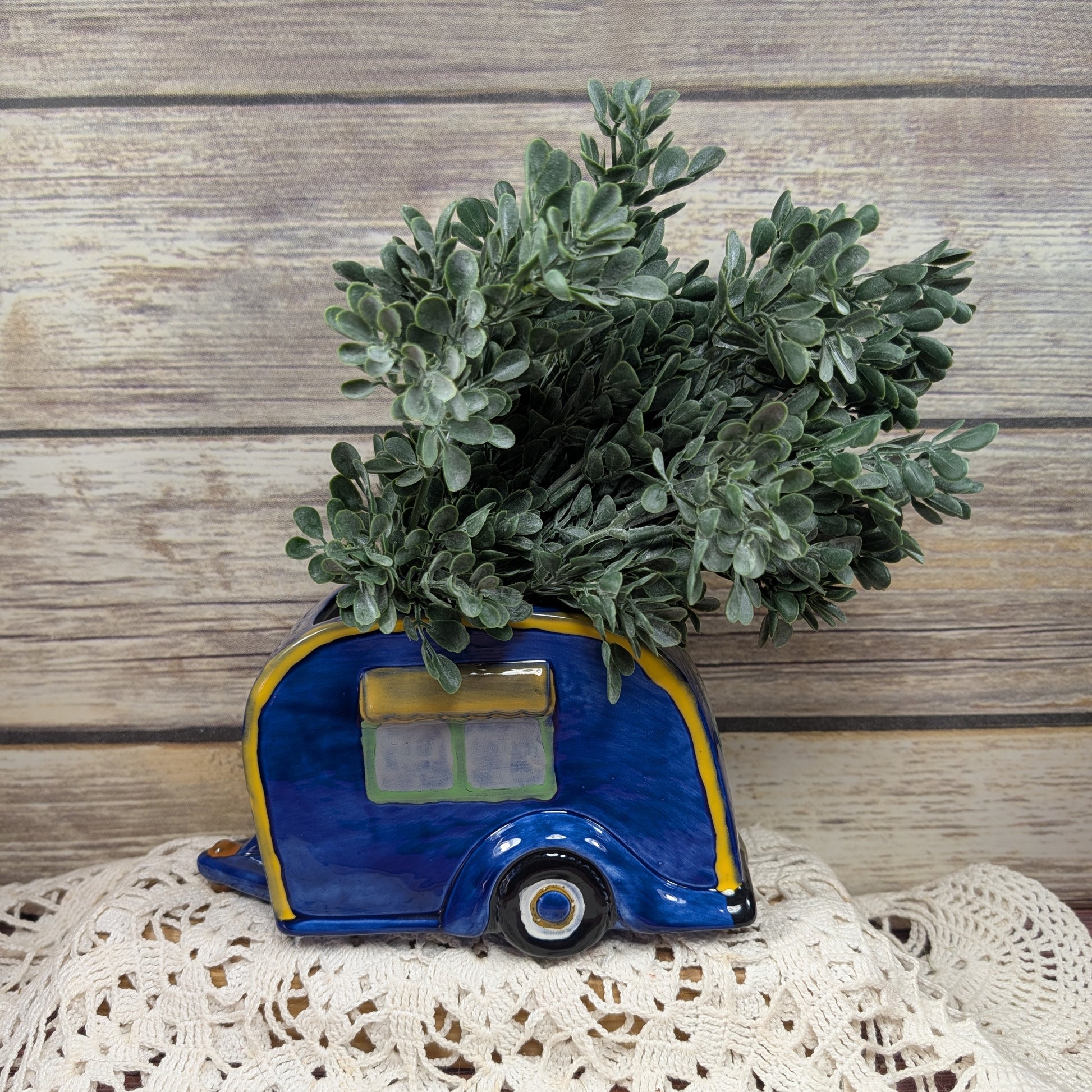 Decorative planter shaped like a blue camper with greenery on a wooden surface.