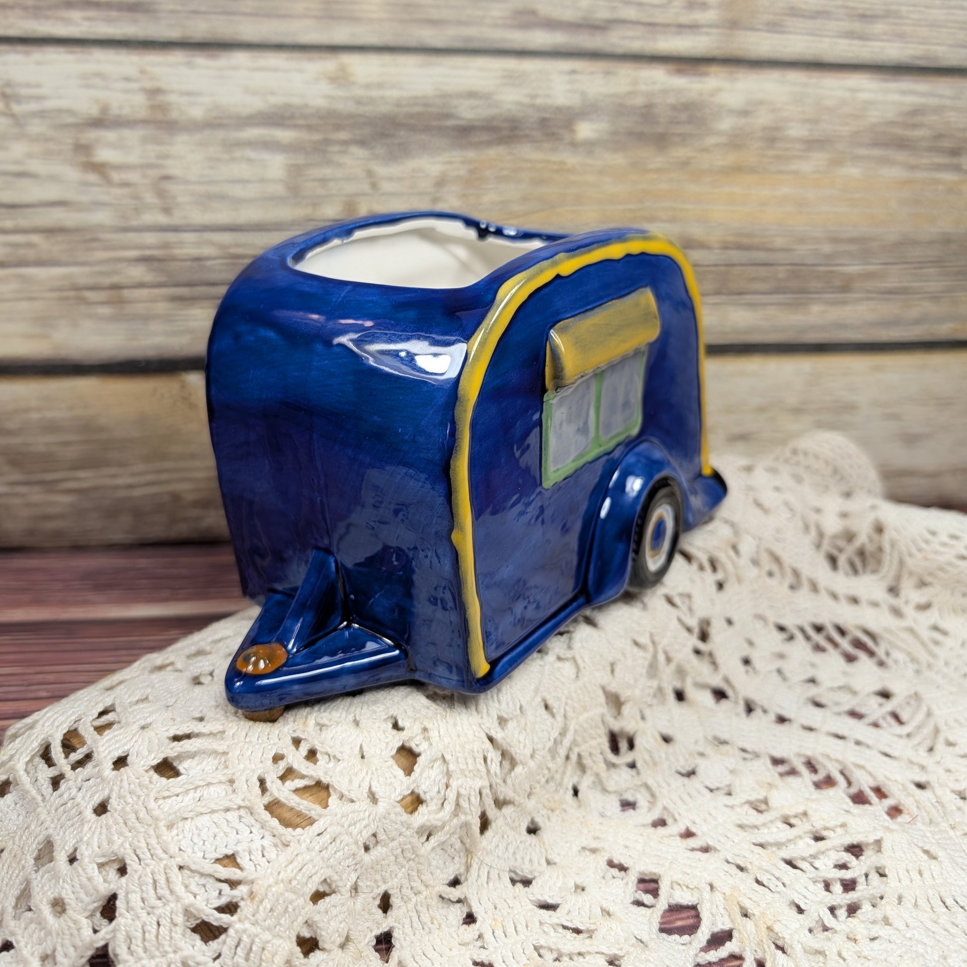 Blue ceramic camper-shaped planter on a textured surface with wooden background