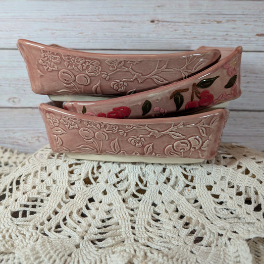 Three pink ceramic bowls with floral patterns stacked on a lace tablecloth.