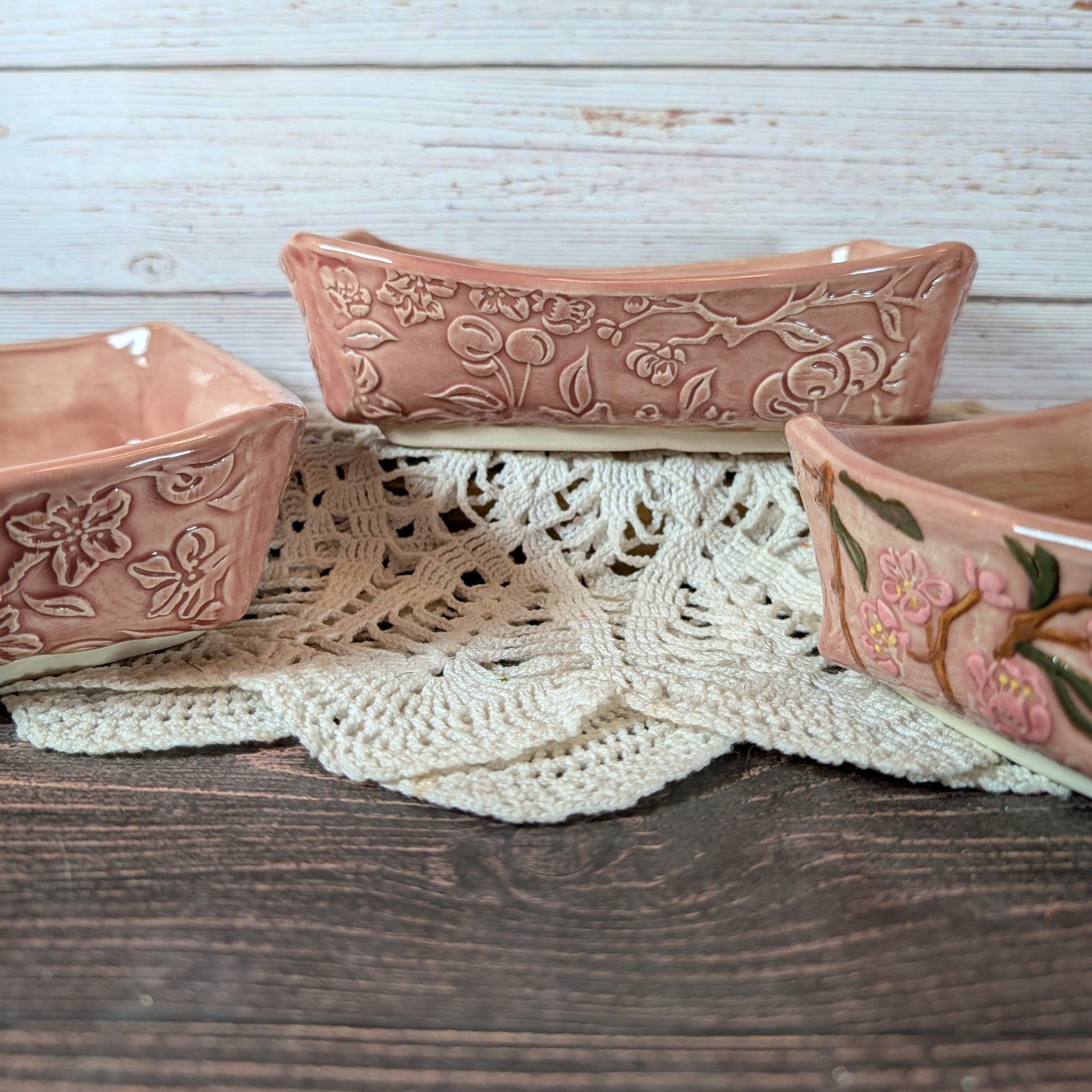 Three pink ceramic bowls with floral patterns on a wooden surface with lace fabric.