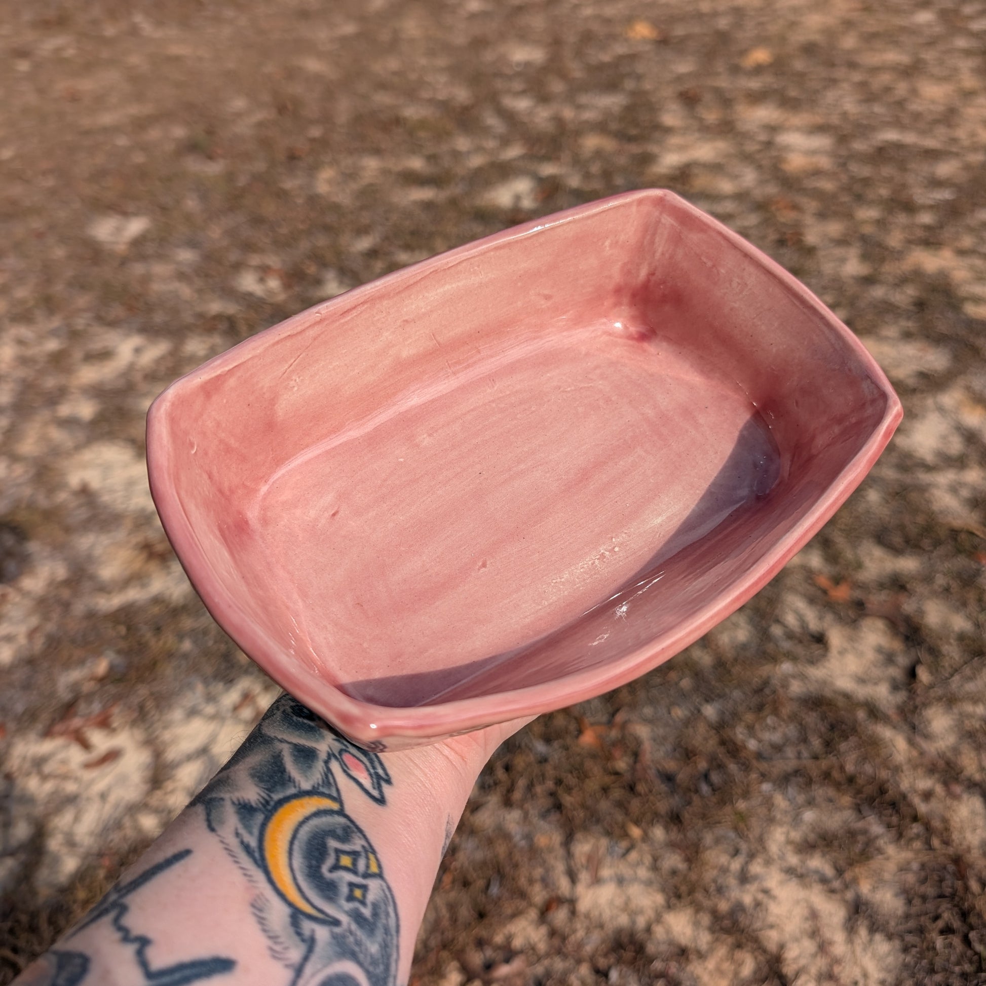 Pink ceramic dish held by a tattooed arm on a textured surface