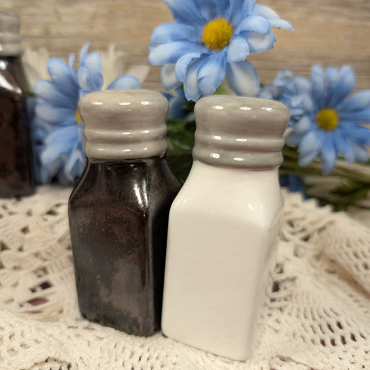 A set of salt and pepper shakers, one black and one white, with a decorative background of blue flowers.
