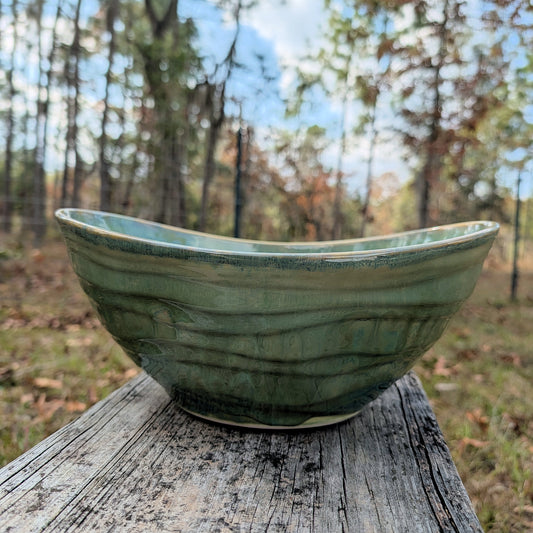 Green ceramic bowl on a wooden log with a forest background