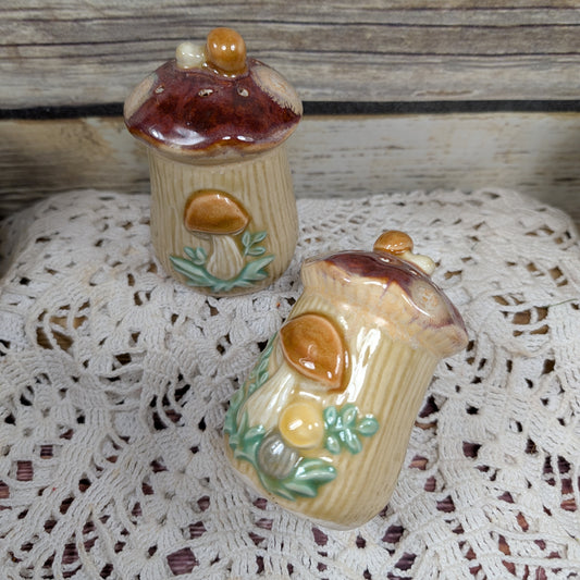 Two ceramic acorn-shaped containers on a lace tablecloth with a wooden background.