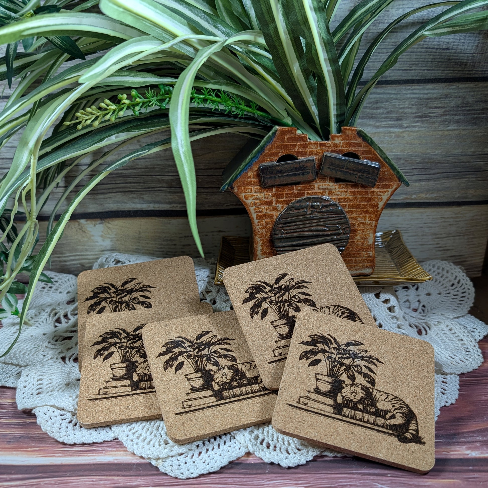 Set of cork coasters with illustrations of a cat and plant on top of books.