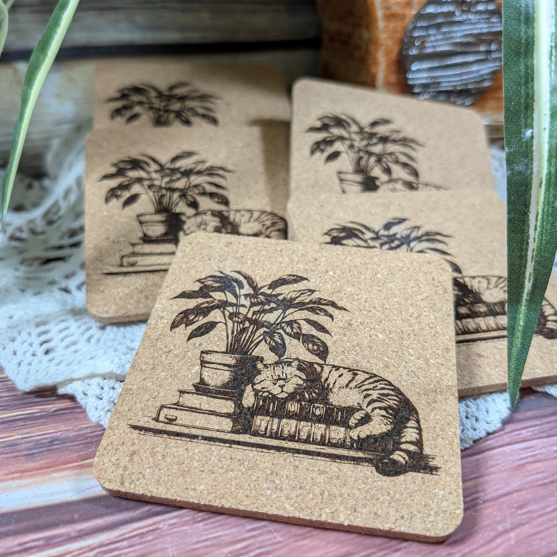 Set of cork coasters with illustrations of a cat and plant on top of books.