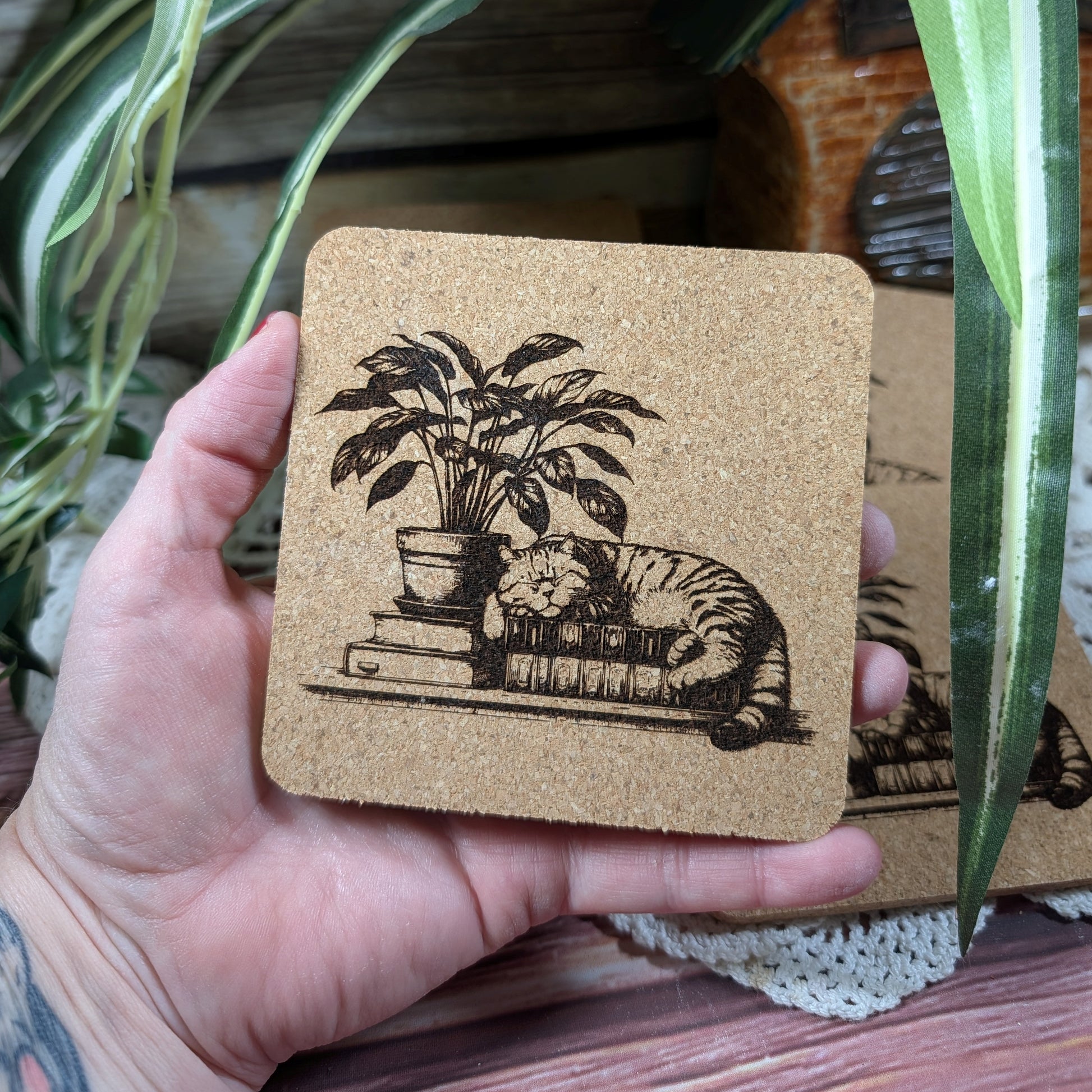 Set of cork coasters with illustrations of a cat and plant on top of books.