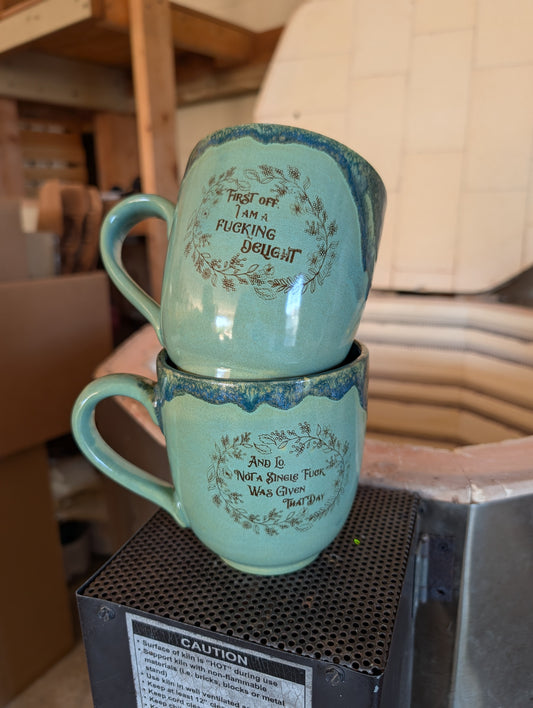Two stacked teal mugs with text on a black surface