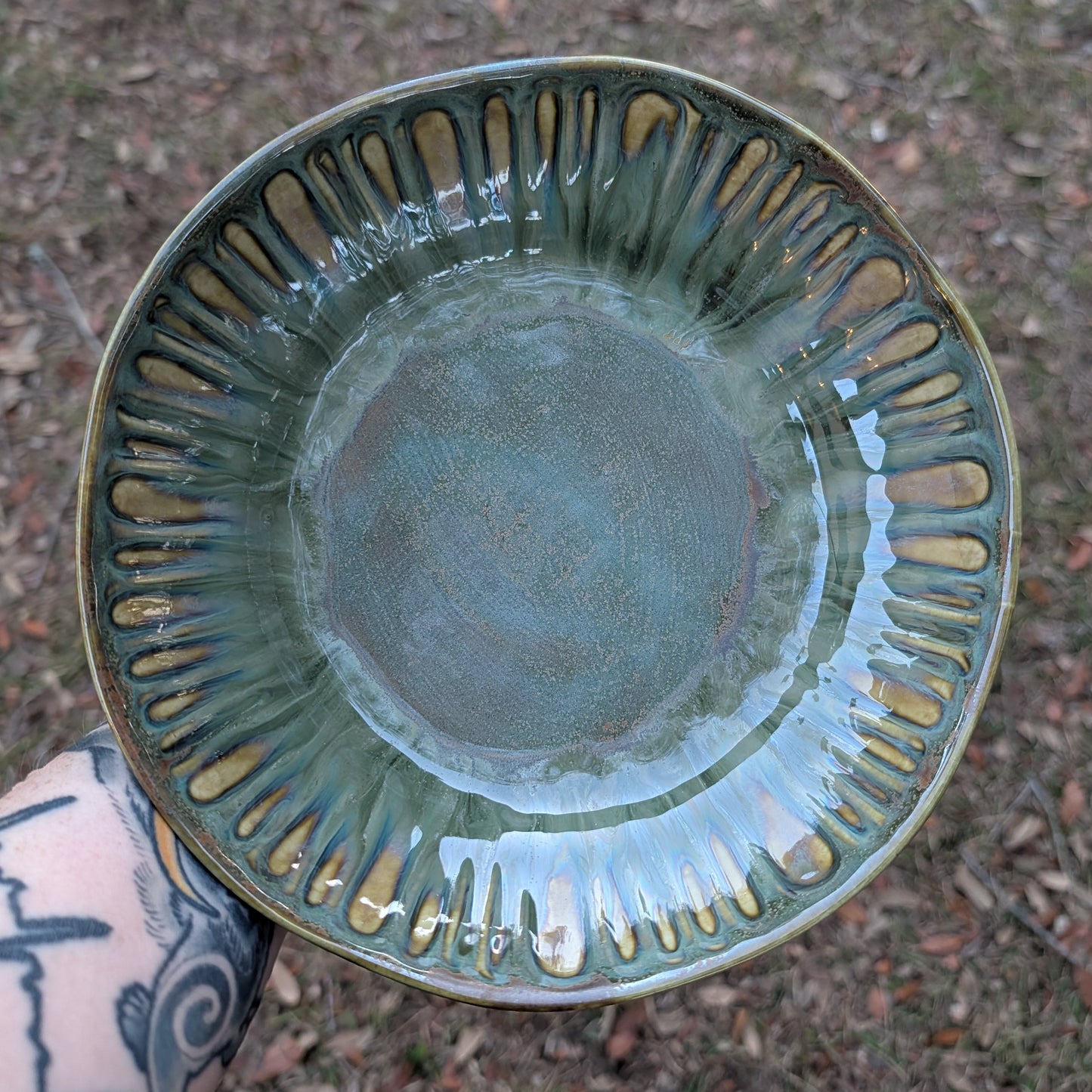 Green ceramic bowl with decorative rim held by a person with tattoos.