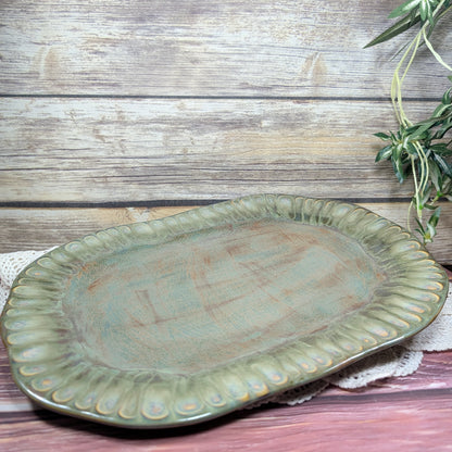 Green ceramic platter on a wooden surface with a plant in the corner