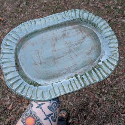 Oval-shaped ceramic dish held by a person with tattoos on a natural background