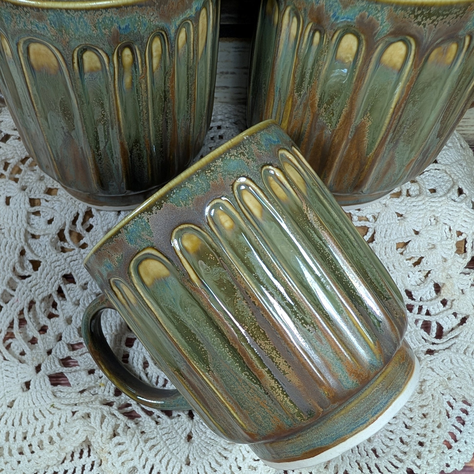 Three ceramic mugs with ribbed design on a lace tablecloth