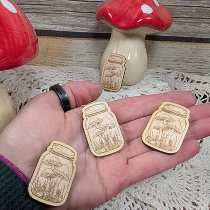 Wooden mushroom and jar magnets held in a hand with decorative mushrooms in the background.