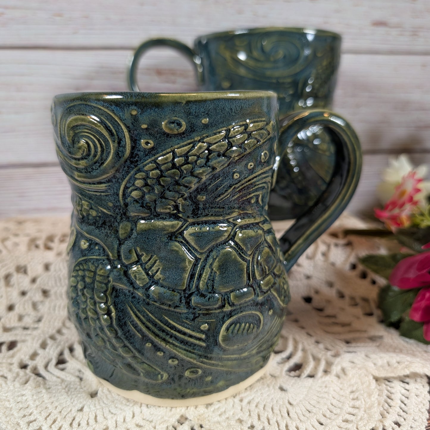 Two green ceramic mugs with detailed designs on a textured surface.