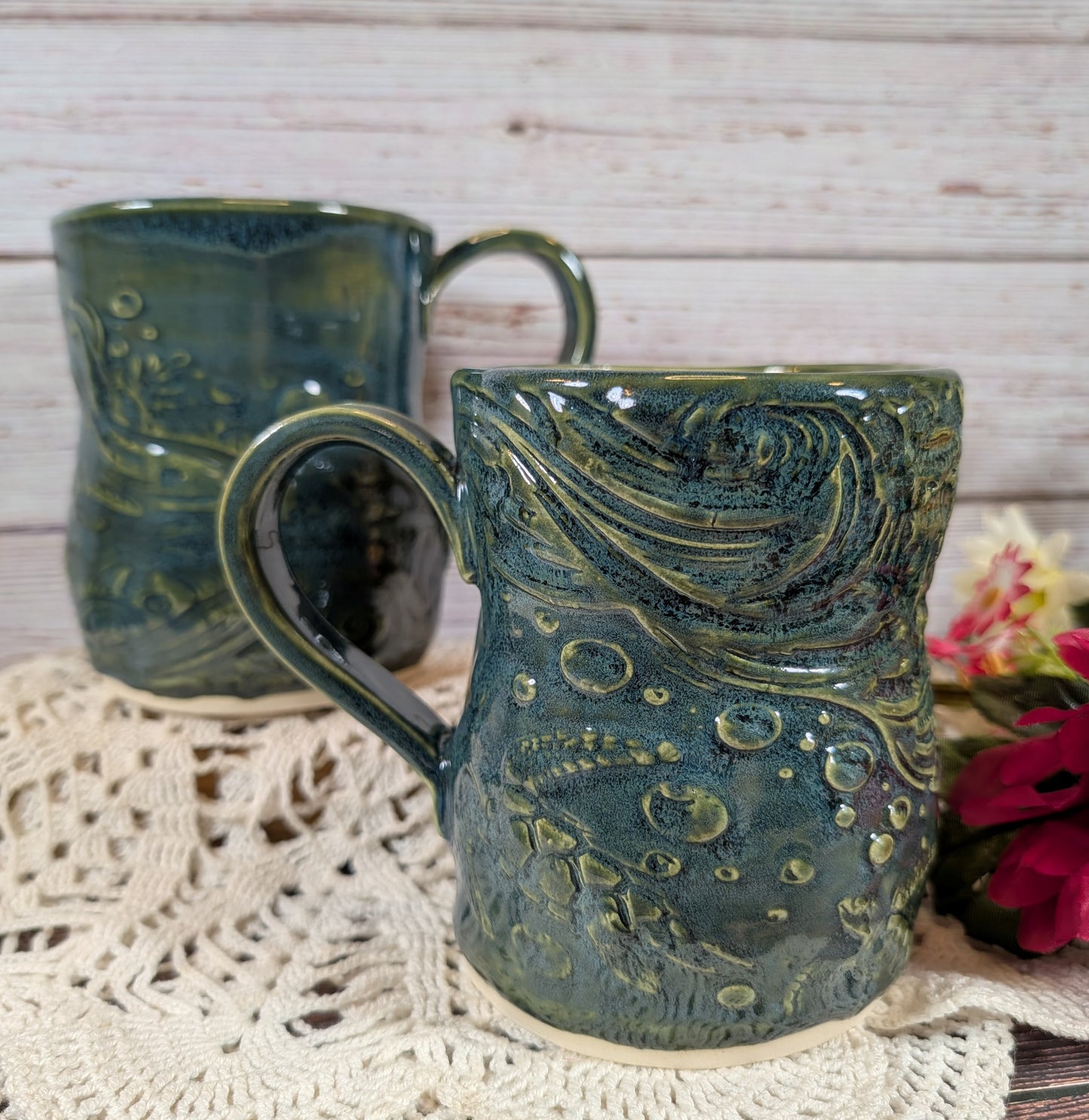 Two green ceramic mugs with textured design on a lace doily.