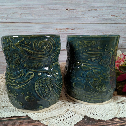 Two green ceramic mugs with intricate patterns on a wooden surface.